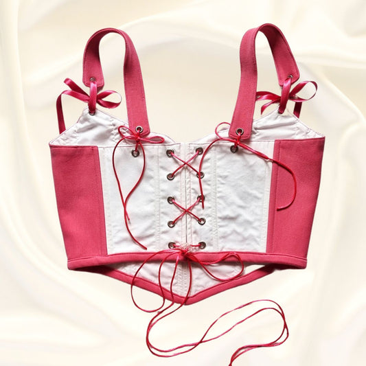 Корсет изработен от розов и бл памучен плат с розови панделки и розова връзка със безцветен стопер. Със сиви метални капси на бежов фон.