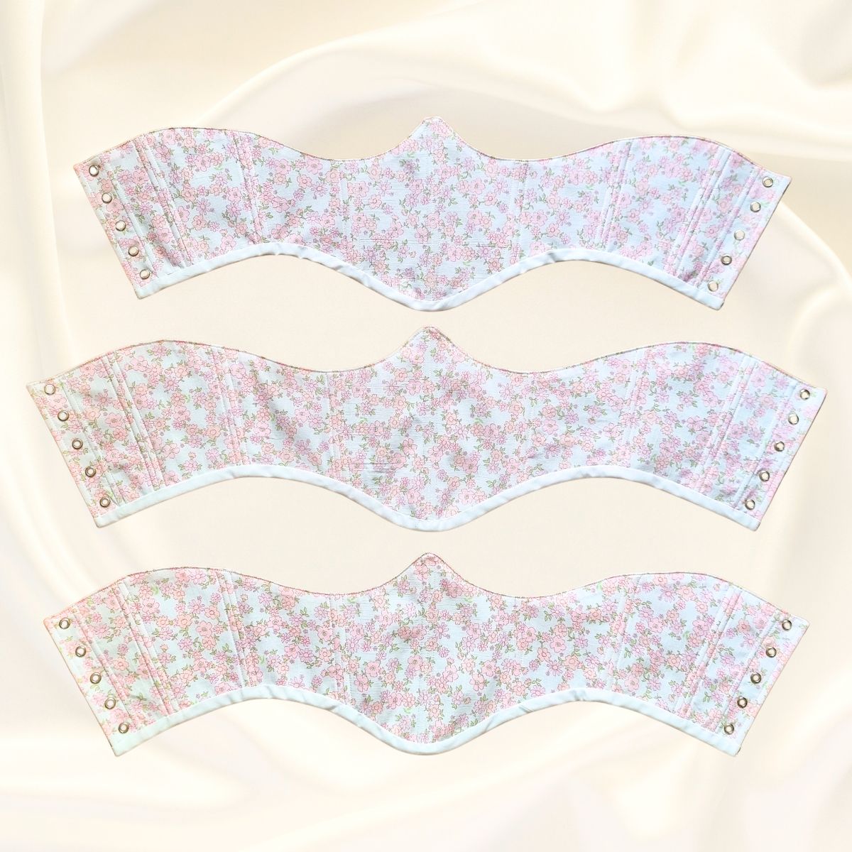 Три дамски кореста тип колан позиционирани един под друг разтворени с капси в бял цвят с розови цветя