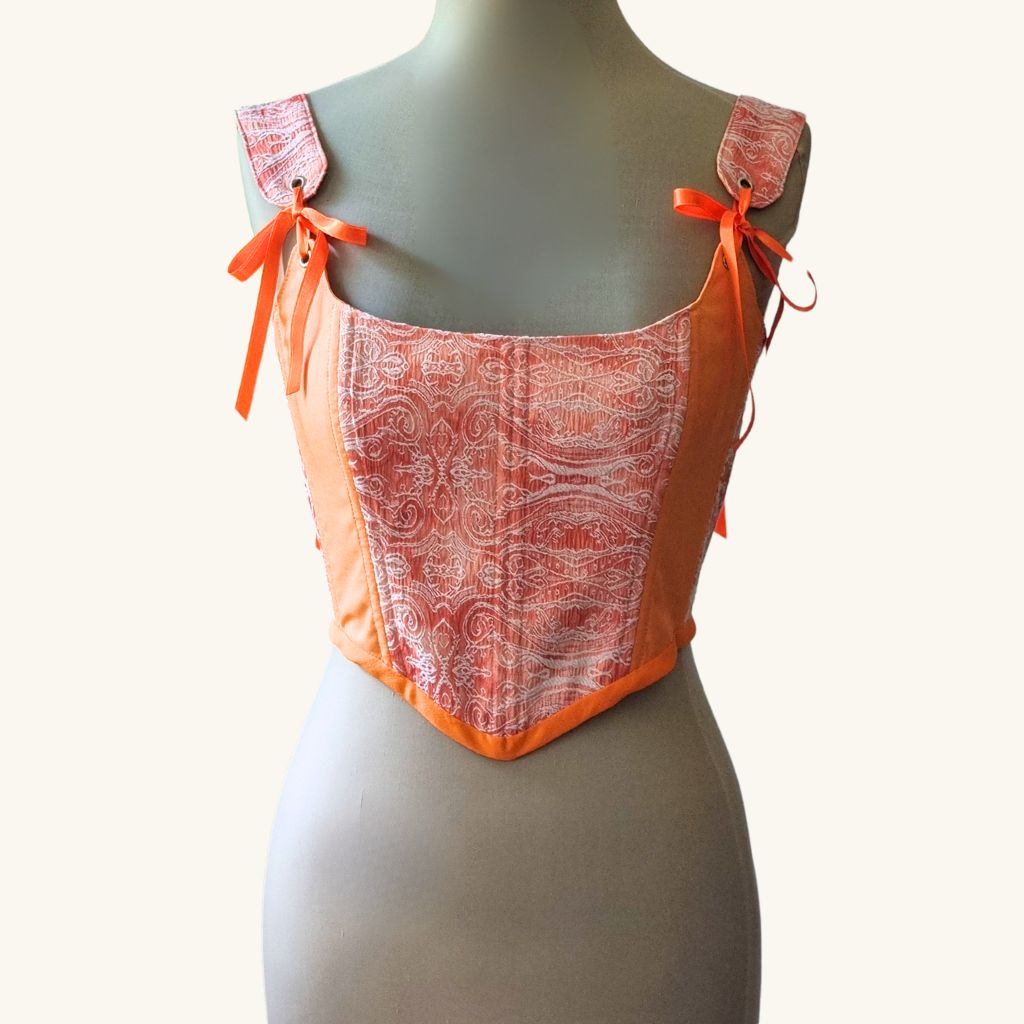 Korset gledka otpred na maneken oranjev rachno izraboten ot pamuk s pandelki i metalni kapsi