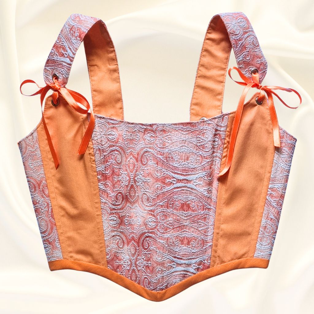 Korset gledka otpred oranjev rachno izraboten ot pamuk s oranjevi sateneni pandelki i mesingovi kapsi